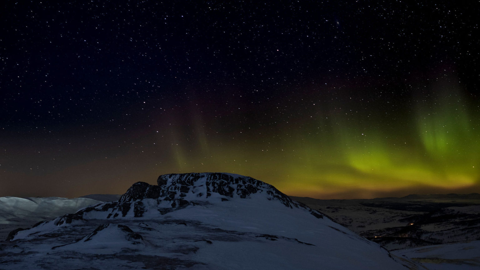 Norrsken och stjärnhimmel över snötäckt fjälltopp