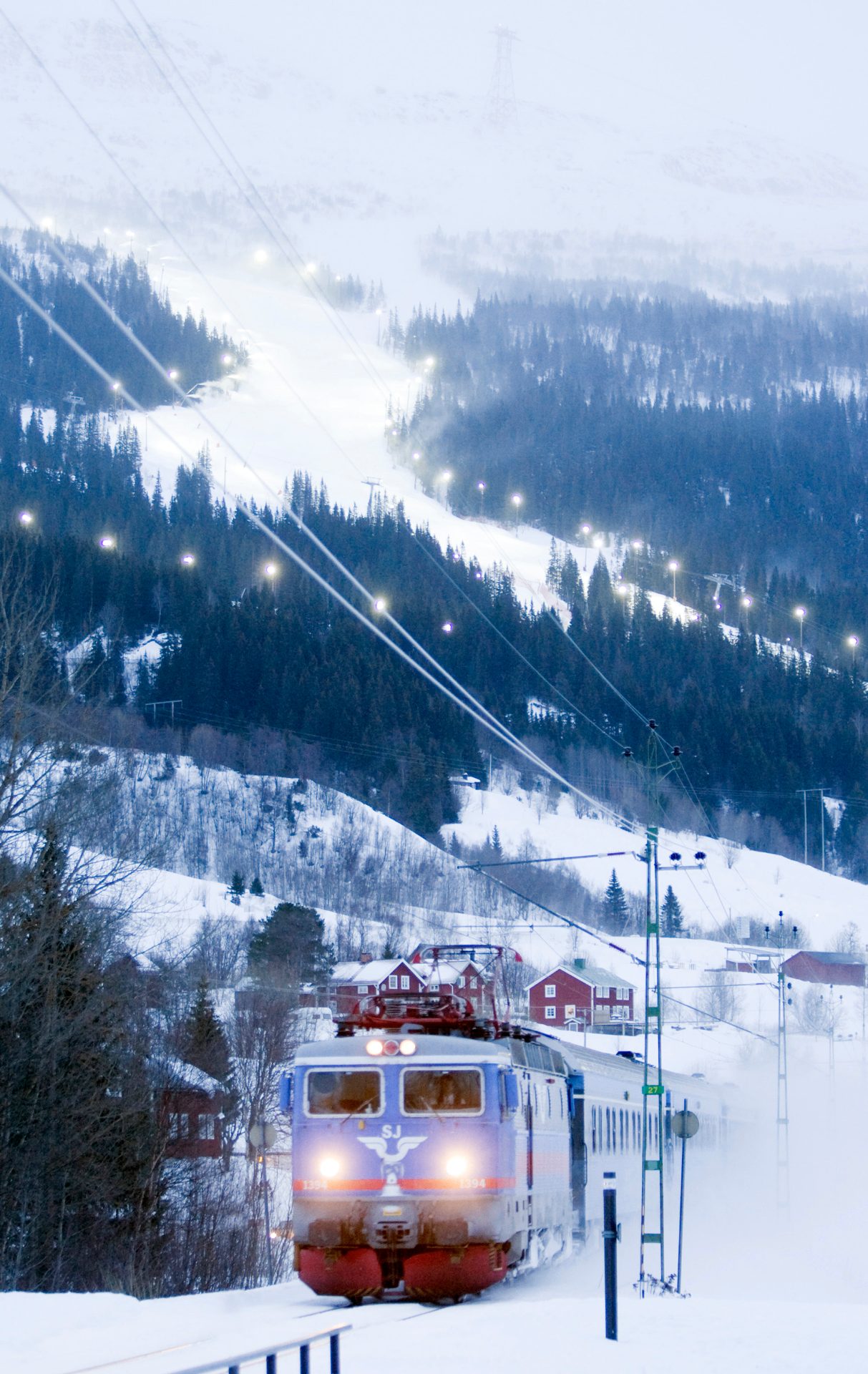 SJ train travelling through snowy Åre with illuminated ski slopes behind it